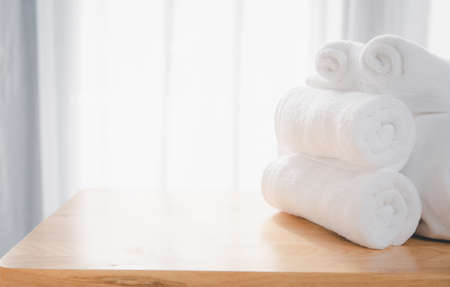 Clean white towels fold on wood table with blurred white bathroom backgroundの写真素材