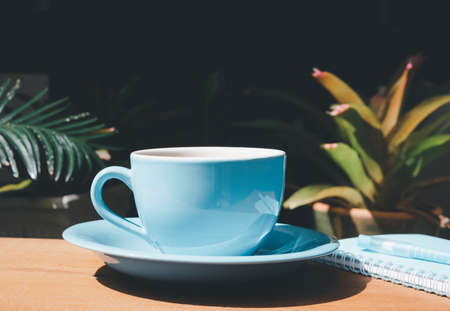 Blue coffee cup with notebook and pen on wood table in gardenの写真素材