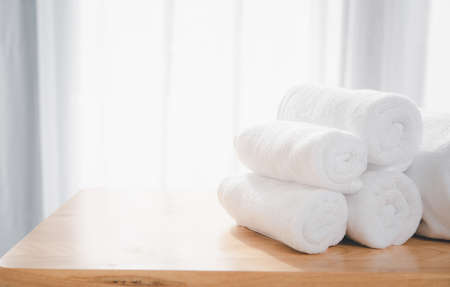 Clean white towels fold on wood table with blurred white bathroom backgroundの写真素材