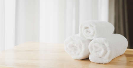 White  soft towels folded on wood table with blurred white bathroom backgroundの写真素材
