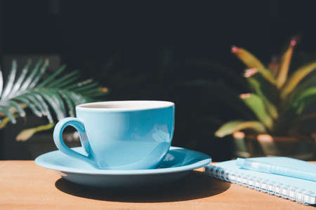 Blue coffee cup with notebook and pen on wood table in gardenの写真素材