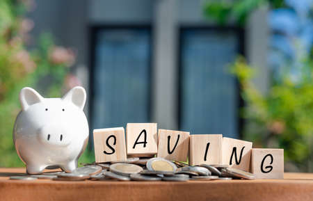 Piggy bank  money coins  and  saving word on wooden cubics  on wood table with nature house backgroundの写真素材