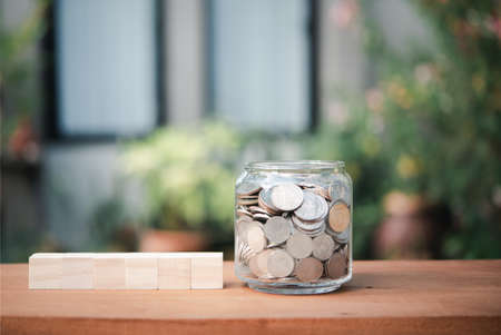 Coins in glass jar and wood cubics on table with green nature backgroundの写真素材