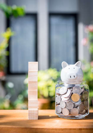 Saving money concepts with coins wood cubics and piggy bank model on table with blurred home backgroundの写真素材