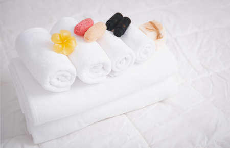 Spa object with  white towels,organic soap,luffa scrub, and plumerai flower candle on clean white bedding.の写真素材