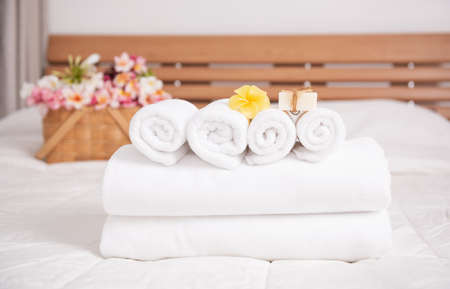 White towels,soap,candle and beautiful frangipani or plumeria flowers in bamboo wooden basket  on modern white bedroomの写真素材