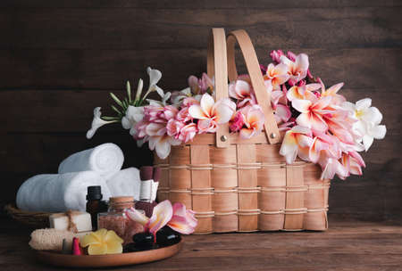 Spa wellness with  organic soap,luffa scrub,compress ball,pink salt,black stones, and plumerai flower basket on wooden tray  over dark wood backgroundの写真素材