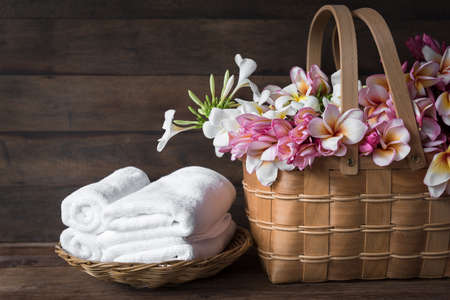 Beautiful frangipani or plumeria flowers in wooden basket and white towels floded on bamboo basket over dark wooden roomの写真素材