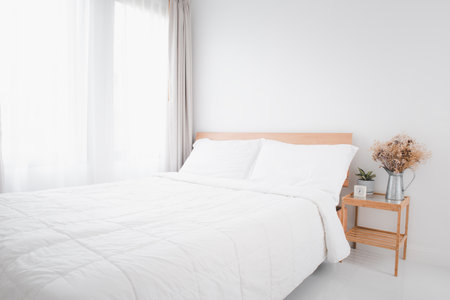 Beautiful white clean cozy bedroom interior with green and dried flowerpot on side wooden tableの写真素材