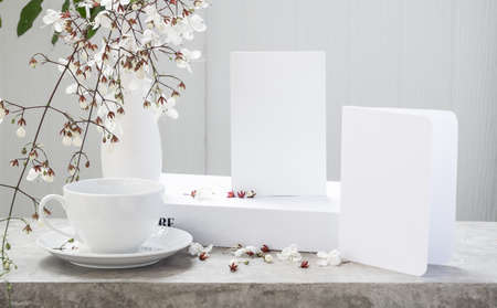 Mock up white  invitation card ,coffee cup and beautiful Nodding Clerodendron flowers in modern vase set on concrete table with white wood background,greeting card in soft tone still lifeの写真素材
