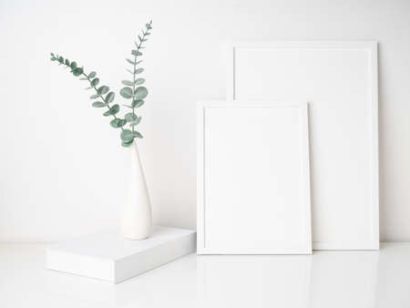Mock up two size white wooden poster frames,book decor with  Eucalyptus  leaves in modern ceramic...