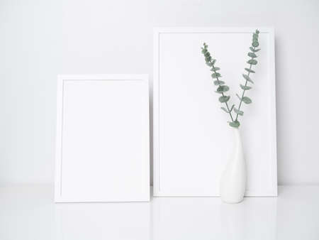Mock up white wooden poster frames decor with  Eucalyptus  leaves in modern  ceramic white vase on...