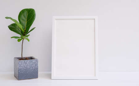 Mininmal stylish mock up poster frame and houseplant in modern cement pot on white wood table and...