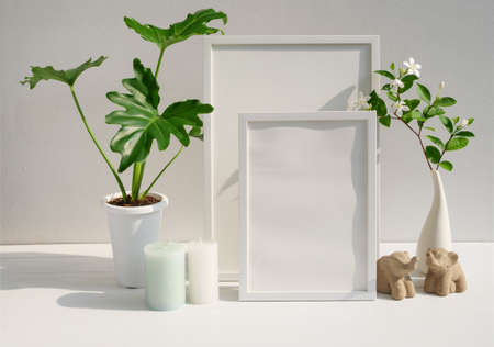Mock up poster frame Philodendron plant Gardenia flower in modern white vase  candle and elephants stasue  on spa  table and cement wall background with long shadowの写真素材