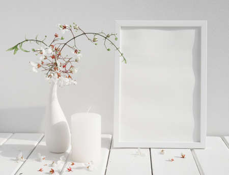 Mock up white invitation poster frame,candle and beautiful Nodding Clerodendron flowers in ceramic vase on wood table white room interior,greeting card in soft tone still lifeの写真素材