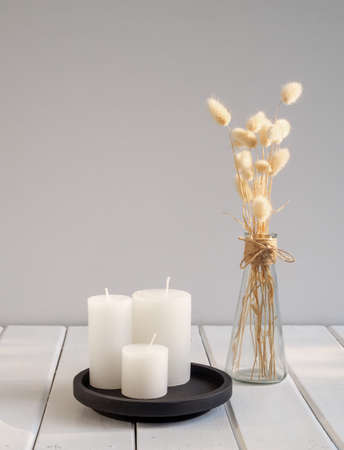 White candles  on black tray and beautiful Lagurus ovatus dried flowers in modern glass vase  composition over white wooden table room interiorの写真素材