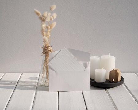 Mock up white invitation card,candles  and beautiful Lagurus ovatus dried flowers in modern glass vase  composition over white wooden table room interiorの写真素材
