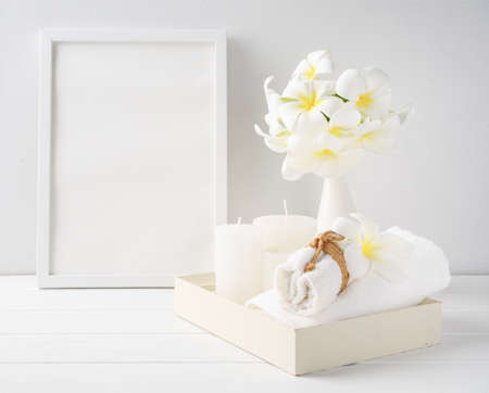 Spa composition,white candles and towel on white wood  tray,mock up poster frame with Plumeria flowers in modern ceramic vase  over wooden table room interior,spa soft tone still lifeの写真素材