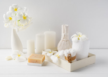 Spa composition massage hearbel ball,plumeria flower in vase,coconut coffee soap,white towels and candle on white wood table background,soft white tone still lifeの写真素材