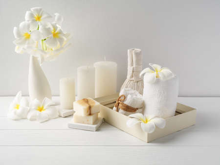 Spa composition massage hearbel ball,plumeria flower in vase,coconut coffee soap,white towels and candle on white wood table background,soft white tone still lifeの写真素材