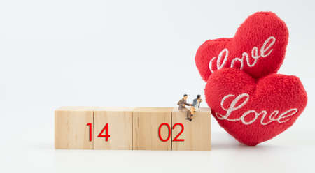 Miniature couple sit on  wooden cubic with 14 February word and beautiful craft red heart  over white background,Valentines conceptの写真素材