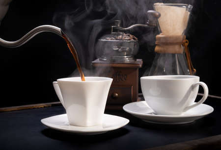 Steam coffee cups with coffee grinder,beans and kettle  on grunge wood table dark backgroundの写真素材