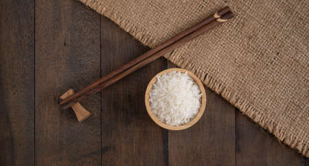 Jasmine  rice in wooden bowl and chopstick on  Sackcloth,burlap hessian  table background  with copy...