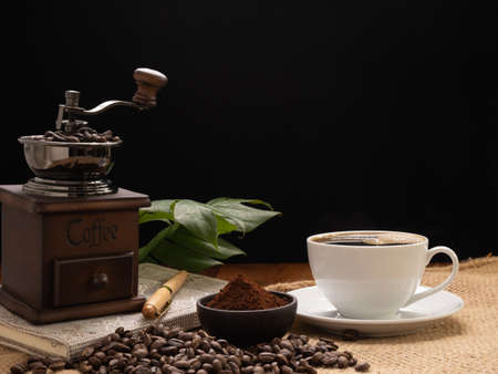 Steam white coffee cup with grinder, roasted beans,coffee ground,green leave  and note book over burlap hessian  on grunge wood table backgroundの写真素材