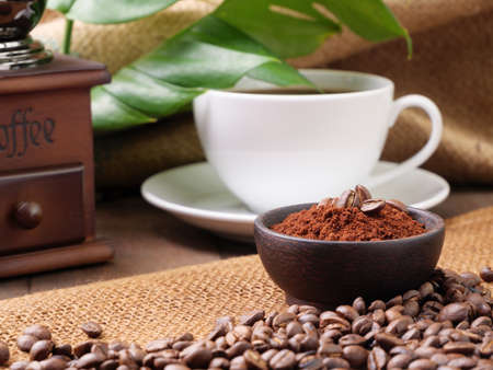 White coffee cups,ground coffee ,roasted coffee beans,grinder, and monstera leave on wooden table with burlap  backgroundの写真素材