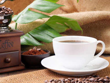 White coffee cups,ground coffee ,roasted coffee beans,grinder, and monstera leave on wooden table with burlap  backgroundの写真素材