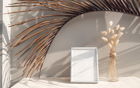 Blank mockup picture frame,coconut palm leaf and dried flower in glass vase on beige table and cement wall backgroundの写真素材