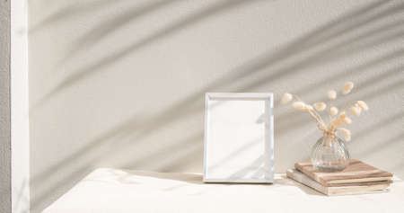Blank mockup picture frame ,craft diary and dried flower in glass vase on beige table and cement wall backgroundの写真素材