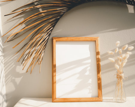 Blank mockup teak wood picture frame,palm leaf  and dried flower in glass vase on beige table and cement wall backgroundの写真素材