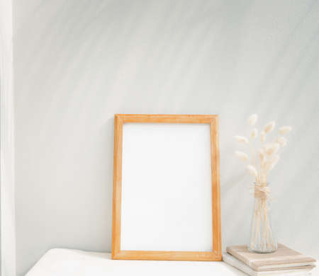 Blank mockup picture frame craft book and dried flower in glass vase on beige table and cement wall backgroundの写真素材