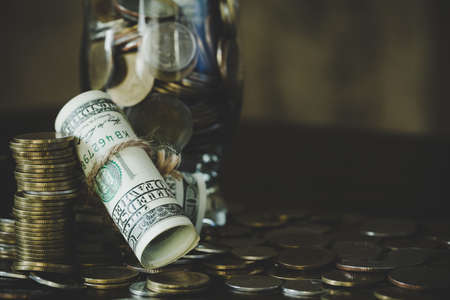 Saving money by dollars with coins in jug glass on dark background