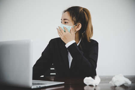 Sick young asian business woman wearing protective face mask having cold fever.Health problems conceptの写真素材