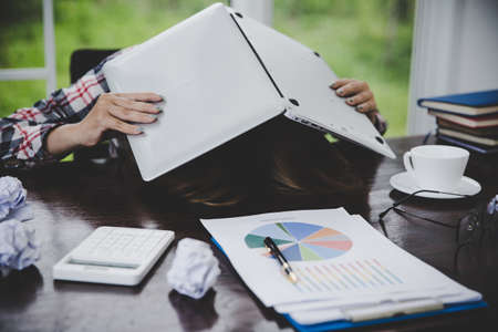 Young frustrated woman working at office desk in front of laptop suffering from chronic daily headaches, treatment online, appointing to a medical consultation, electromagnetic radiation, sick payの写真素材
