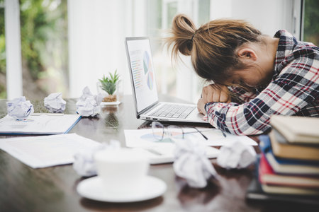 Tired businesswoman working on a computer Portrait of stressed young woman comfortably with headache at desk. Exhausted business woman working on laptop at office.の写真素材