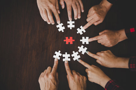 High Angle View Of Businesspeople Hand Solving Jigsaw Puzzle On Wooden Deskの写真素材