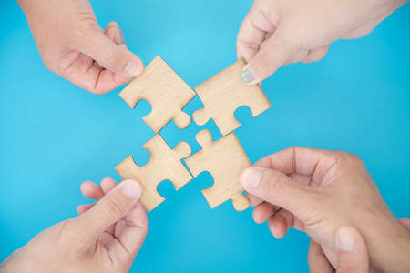High Angle View Of Businesspeople Hand Solving Jigsaw Puzzle On Blue Backgroundの写真素材