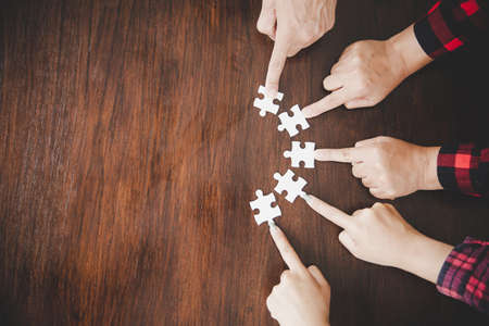 High Angle View Of Businesspeople Hand Solving Jigsaw Puzzle On Wooden Deskの写真素材