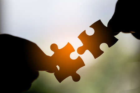 Closeup hand of woman connecting jigsaw puzzle with sunlight effect, Business solutions, success and strategy conceptの写真素材