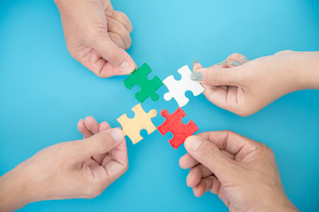 High Angle View Of Businesspeople Hand Solving Jigsaw Puzzle On Blue Backgroundの写真素材