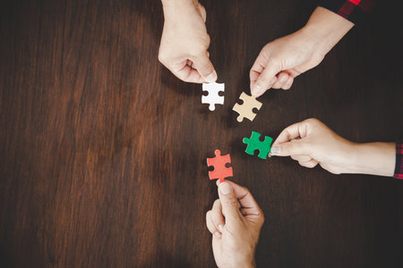 High Angle View Of Businesspeople Hand Solving Jigsaw Puzzle On Wooden Deskの写真素材