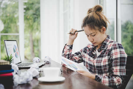 Tired businesswoman working on a computer Portrait of stressed young woman comfortably with headache at desk. Exhausted business woman working on laptop at office.の写真素材