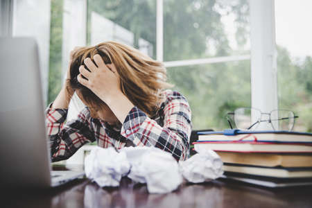 Young frustrated woman working at office desk in front of laptop suffering from chronic daily...