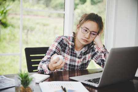 Tired businesswoman working on a computer Portrait of stressed young woman comfortably with headache at desk. Exhausted business woman working on laptop at office.の写真素材