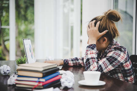 woman sitting down, his face unsettled. At the computer desk she has headaches and stress. Cause of hard work and insufficient rest.の写真素材