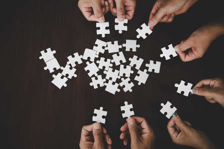 High Angle View Of Businesspeople Hand Solving Jigsaw Puzzle On Wooden Deskの写真素材