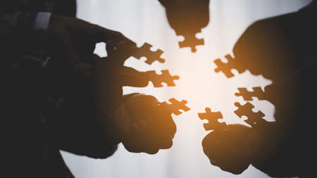 Closeup hand of business people connecting jigsaw puzzle with sunlight effect, Business solutions and represent team support and help concept, success and strategy conceptの写真素材